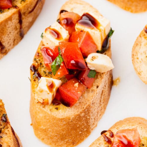 A slice of gluten-free toasted baguette topped with tomato, mozzarella, basil and balsamic glaze.