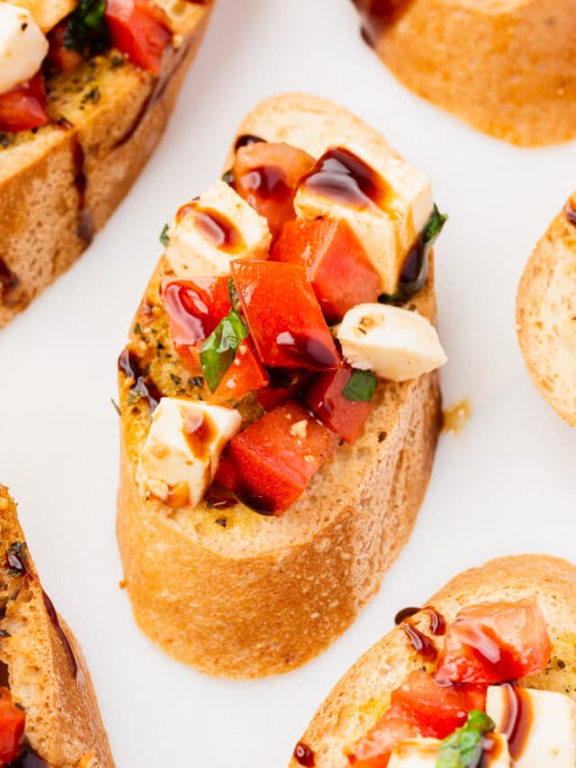 A slice of gluten-free toasted baguette topped with tomato, mozzarella, basil and balsamic glaze.