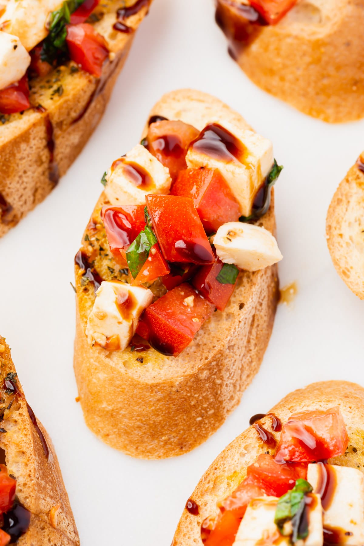 A slice of gluten-free toasted baguette topped with tomato, mozzarella, basil and balsamic glaze.