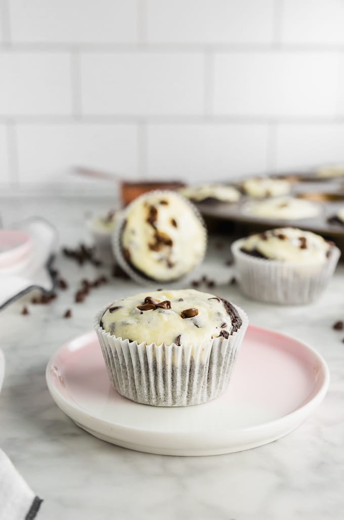 A photo of a gluten-free black bottom cupcake with cheesecake filling and topped with mini chocolate chips on a marble table. 