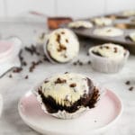 A photo of a gluten-free black bottom cupcake with cheesecake filling and topped with mini chocolate chips on a marble table.