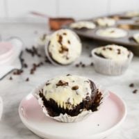 A photo of a gluten-free black bottom cupcake with cheesecake filling and topped with mini chocolate chips on a marble table.