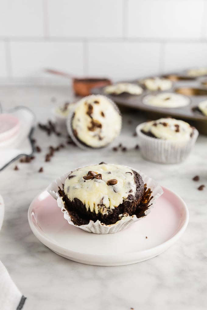 A photo of a gluten-free black bottom cupcake with cheesecake filling and topped with mini chocolate chips on a marble table. 