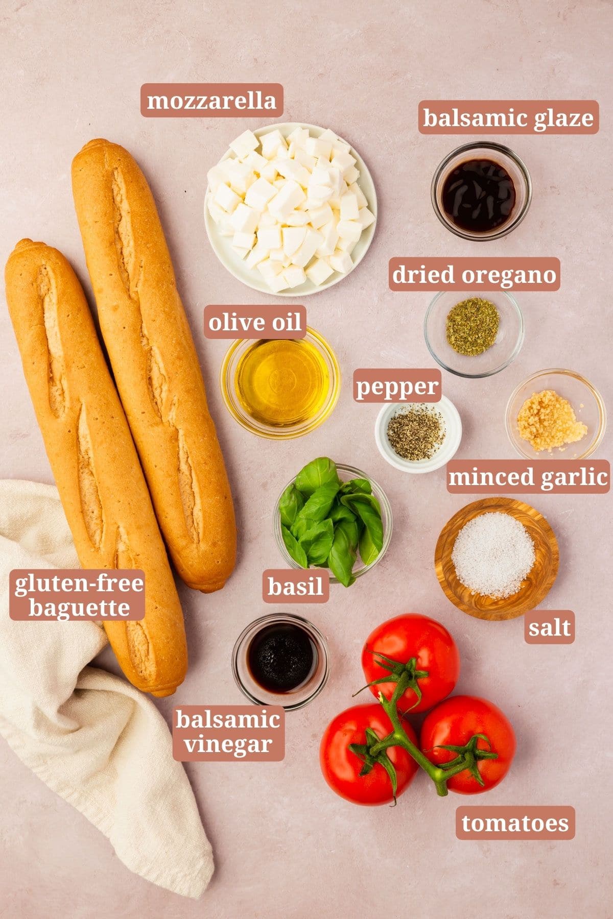 Ingredients for making bruschetta with mozzarella on a pink table: gluten-free baguette, mozzarella, balsamic glaze, basil, olive oil, pepper, oregano, garlic, salt, tomatoes and balsamic vinegar.