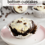 A photo of a gluten-free black bottom cupcake with cheesecake filling and topped with mini chocolate chips with the muffin liner unwrapped on a marble table.