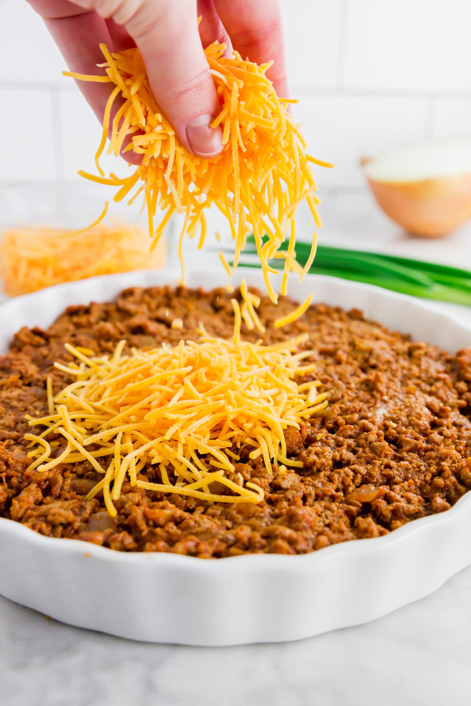 A photo of shredded cheddar cheese being sprinkled over turkey chili for gluten-free chili dip. 