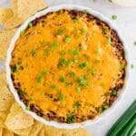 A photo of a tart pan filled with chili cheese dip topped with green onions.
