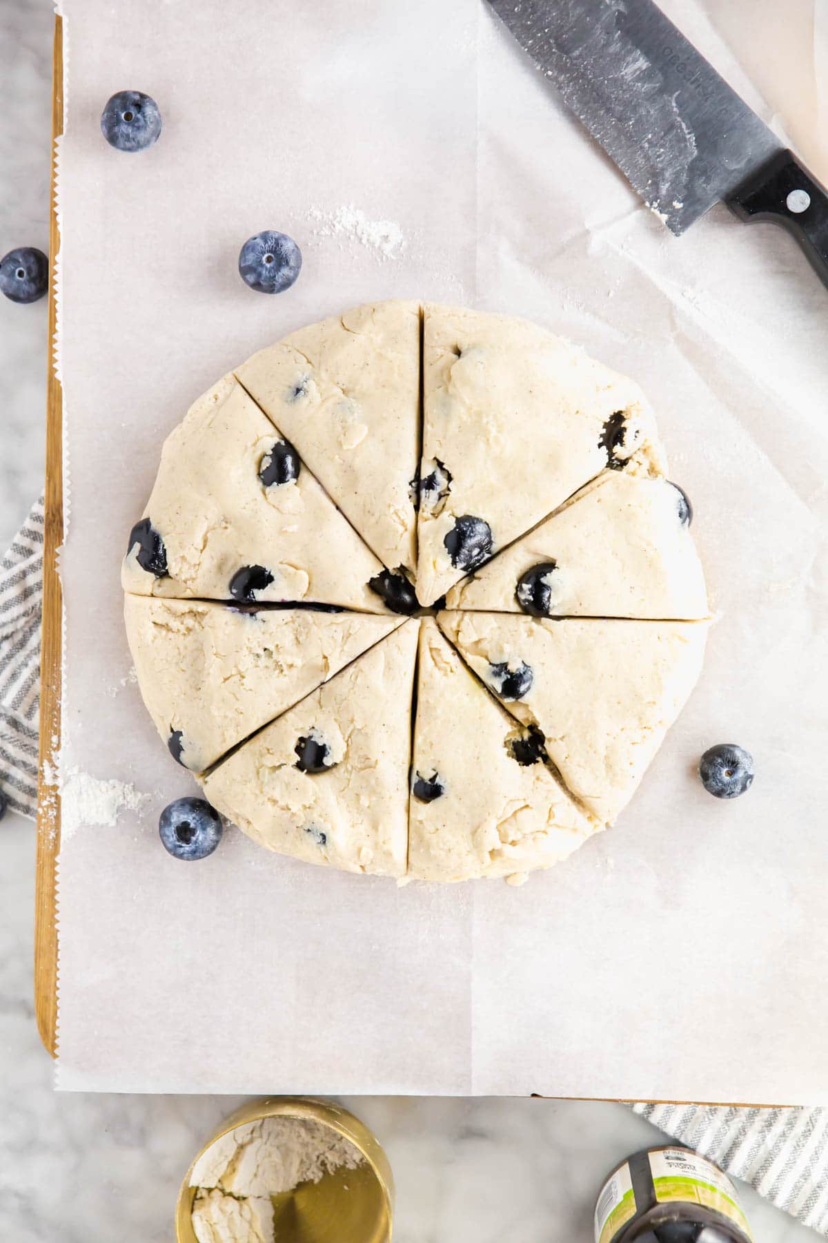 A photo of a disk of gluten-free blueberry scone dough sliced into eight wedges. 