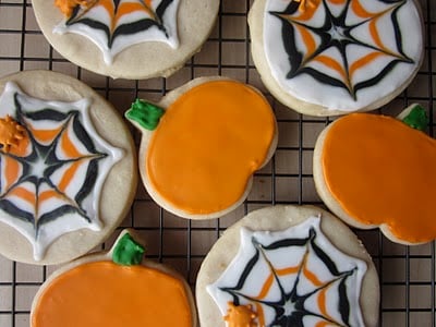 A cooling rack with orange and black spider web and pumpkin decorated sugar cookies.