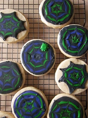 A cooling rack with black, purple and green spider web decorated sugar cookies.