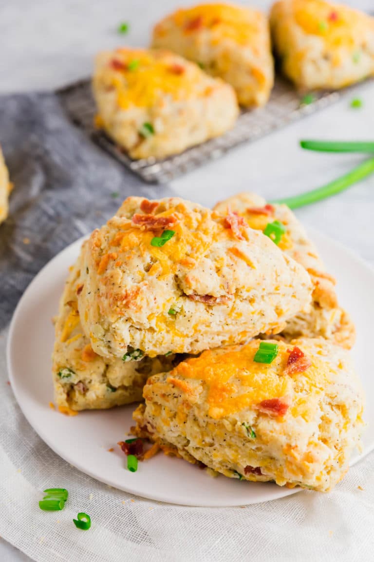 A white plate with gluten-free bacon cheddar scones stacked on top with green onions and bacon scattered.