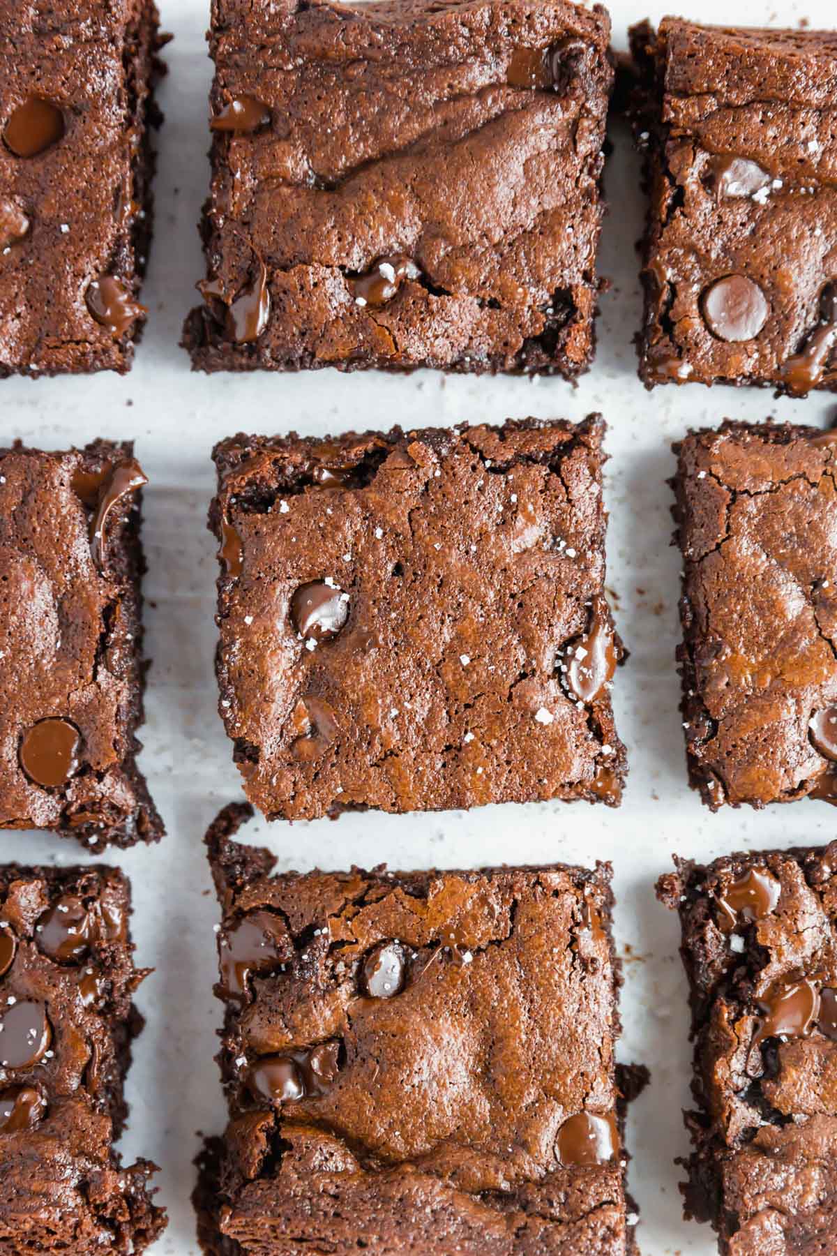 An overhead image showing a close up of 9 almond flour brownies sliced in squares topped with flaky salt. 