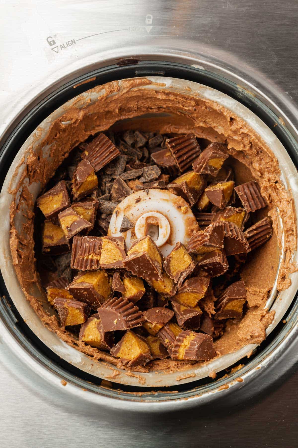Chocolate ice cream topped with peanut butter cups in the bowl of an ice cream maker.