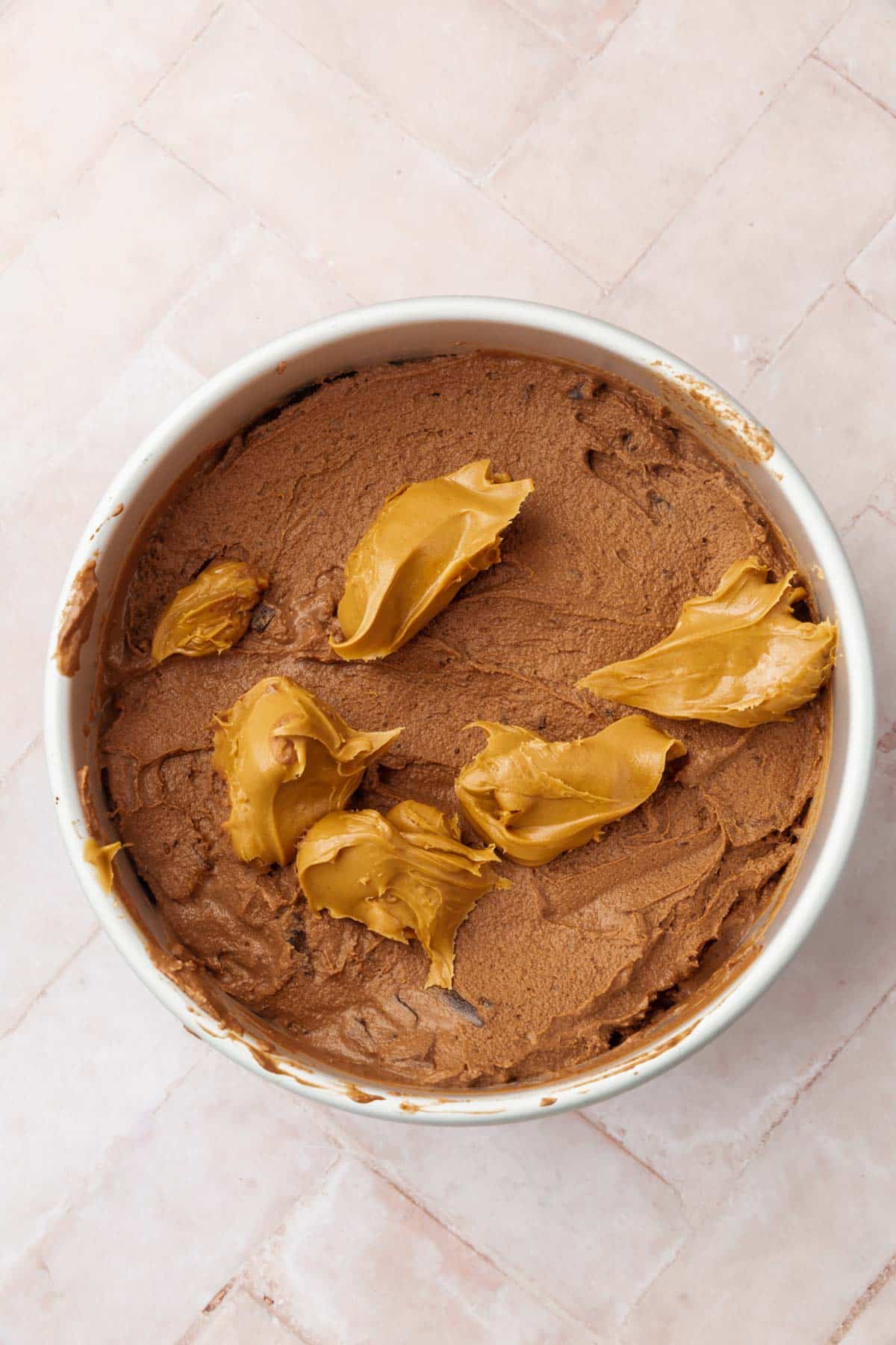 A round pan with chocolate ice cream topped with dollops of peanut butter on it.