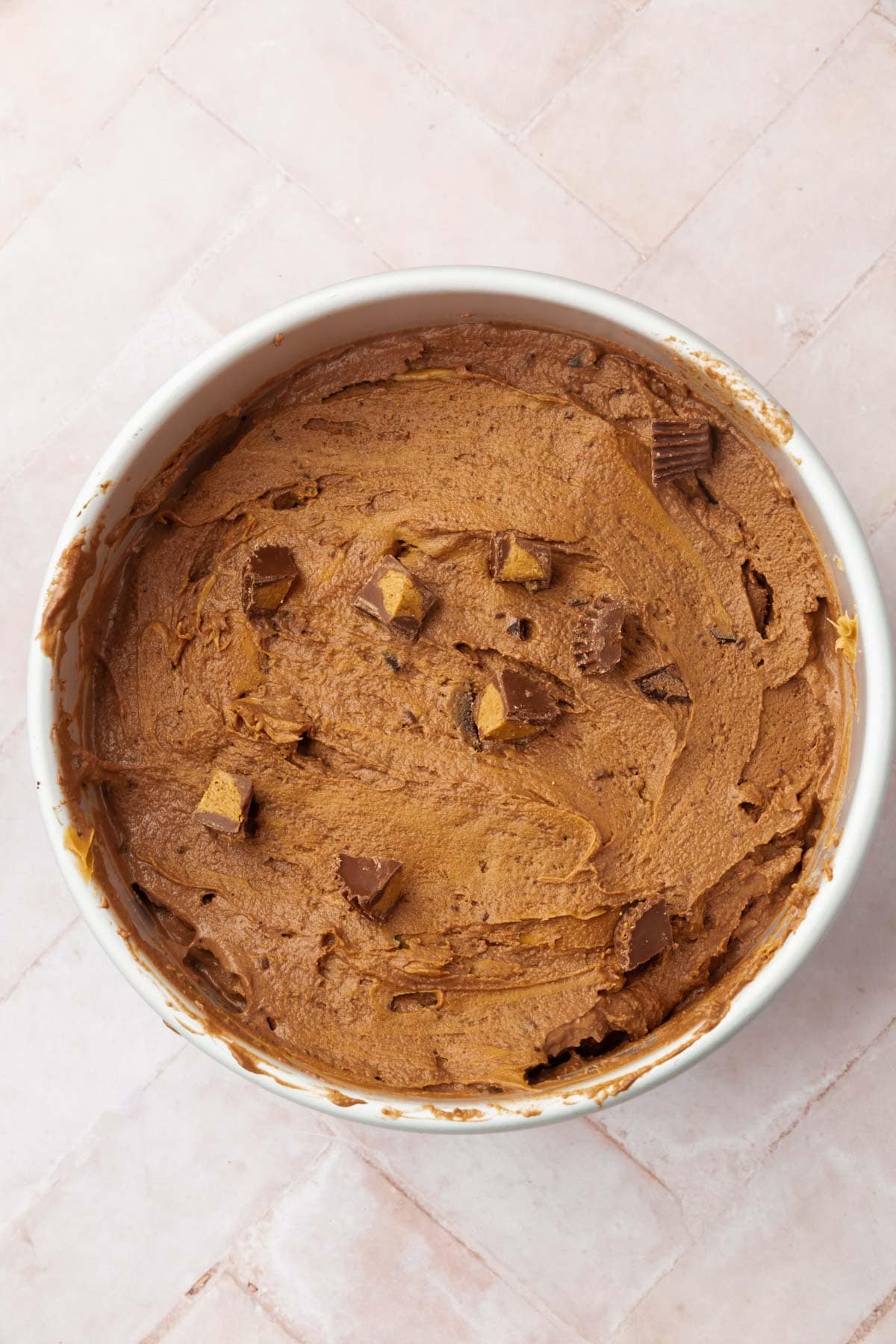 A round pan with chocolate peanut butter ice cream in it topped with chopped up peanut butter cups.
