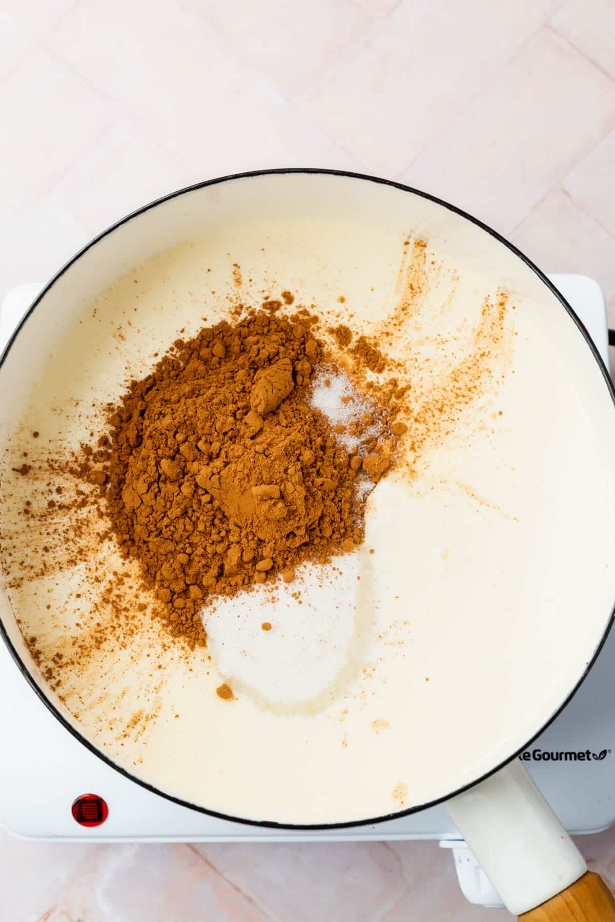 A saucepan on an electric burner filled with heavy cream, milk, cocoa powder and granulated sugar.