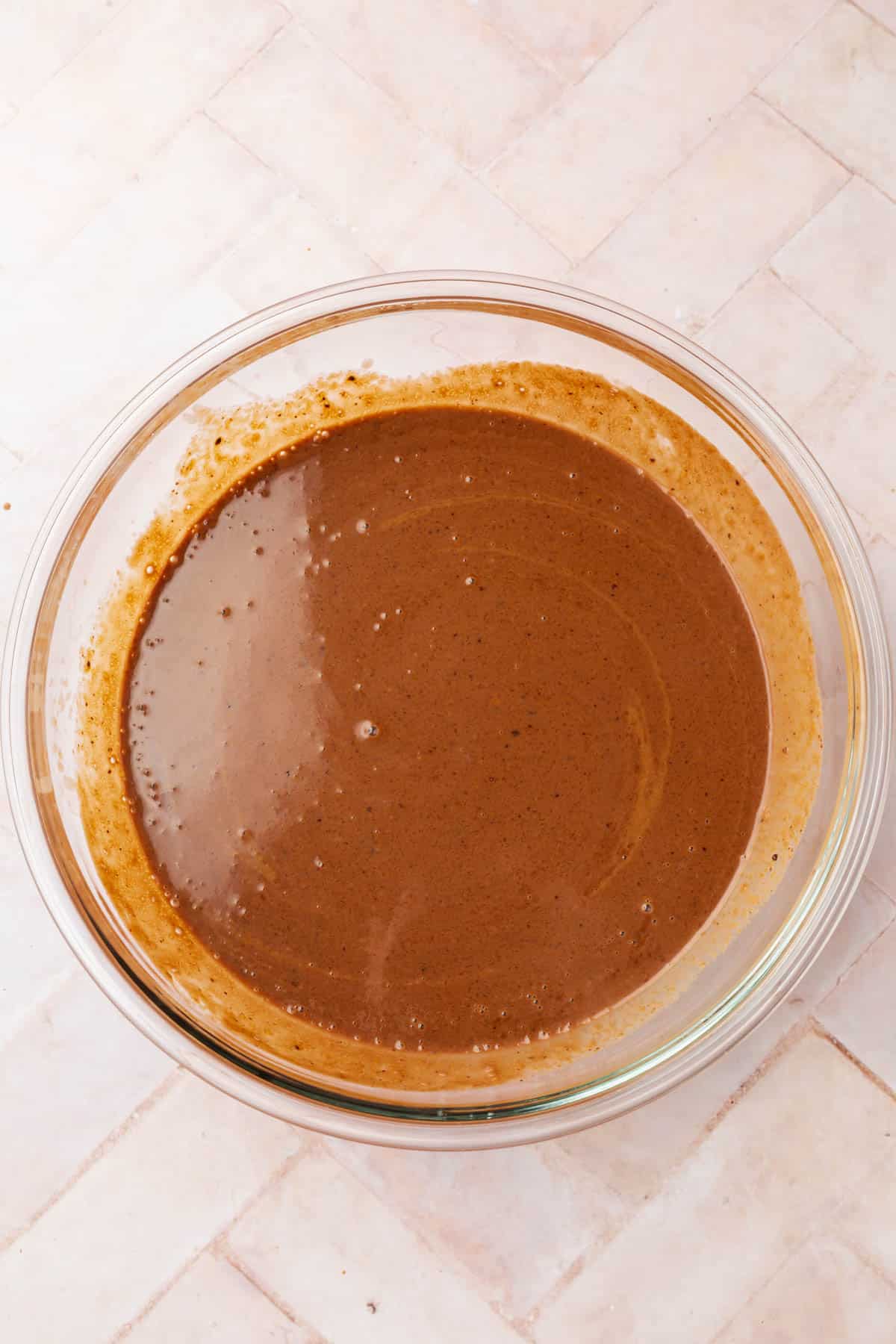 A glass bowl on a pink table with chocolate ice cream custard in it.