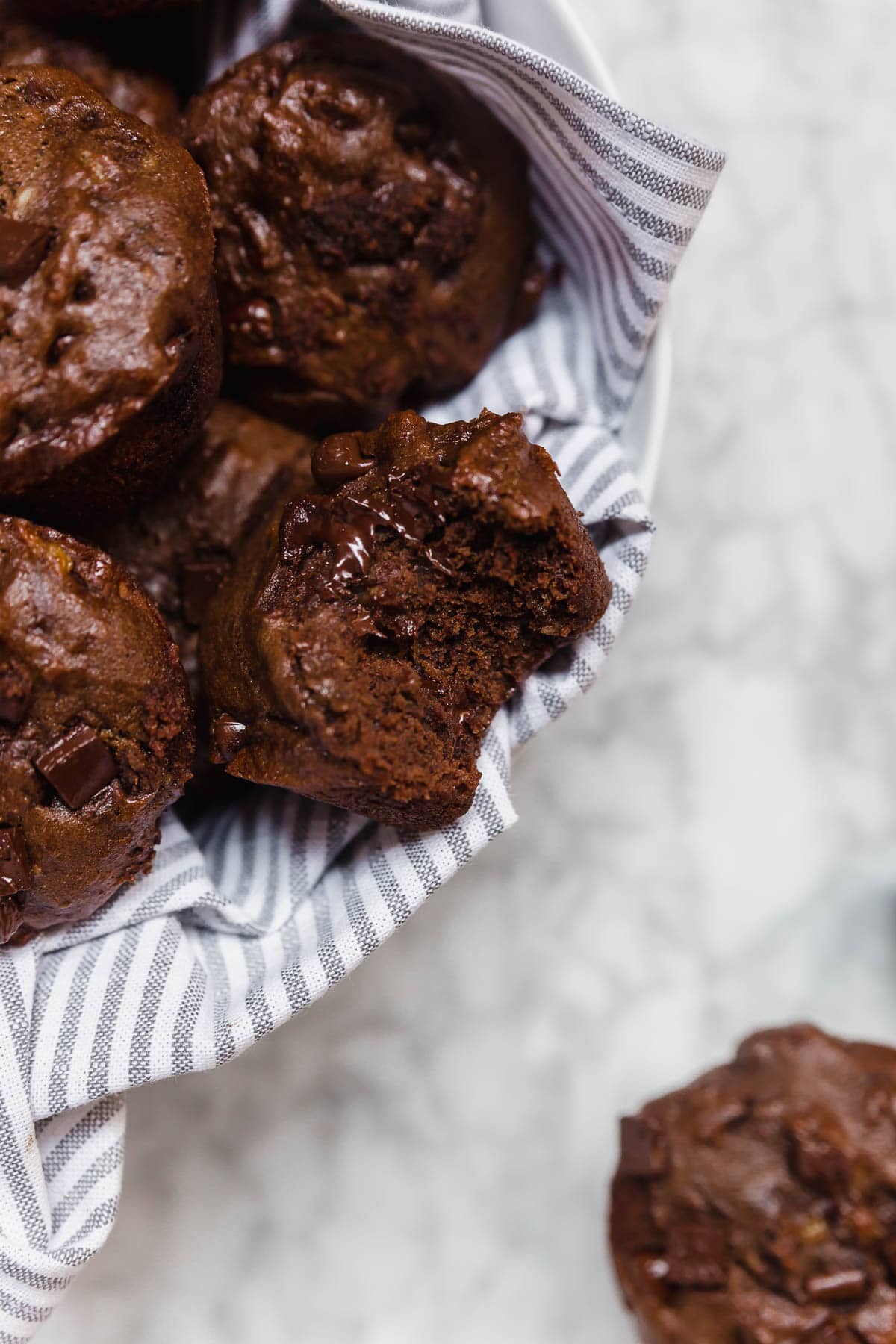 A basket of gluten-free vegan double chocolate banana muffins on a marble table. 