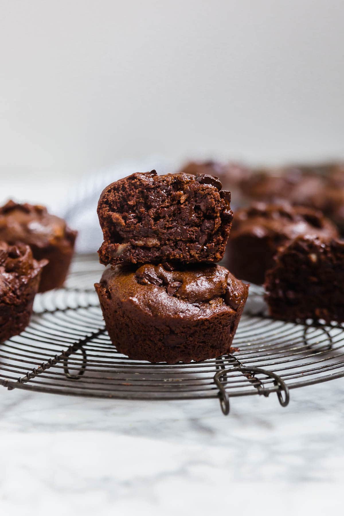A stack of two double chocolate chip muffins on a cooling rack with the top muffin cut in half to see the inside.