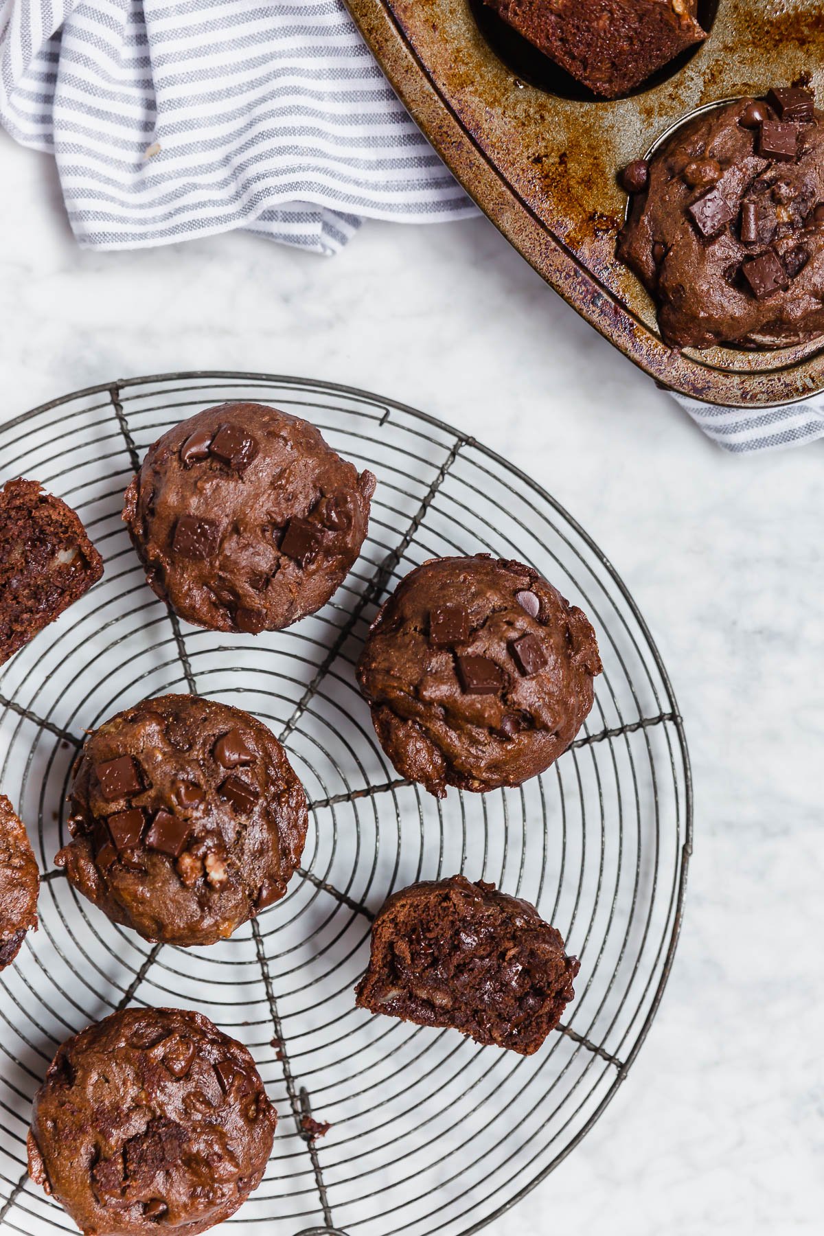 A round baking rack with gluten-free double chocolate chunk banana muffins on a white marble table. 