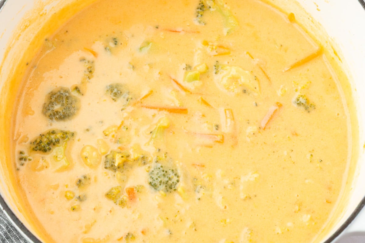 Pot of gluten-free broccoli cheddar soup, smooth and creamy with visible broccoli and carrot pieces.