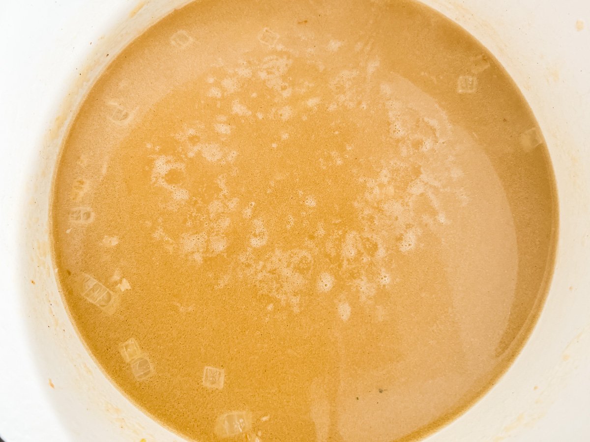 Whisking broth into the roux to create a smooth, golden soup base in a white Dutch oven.