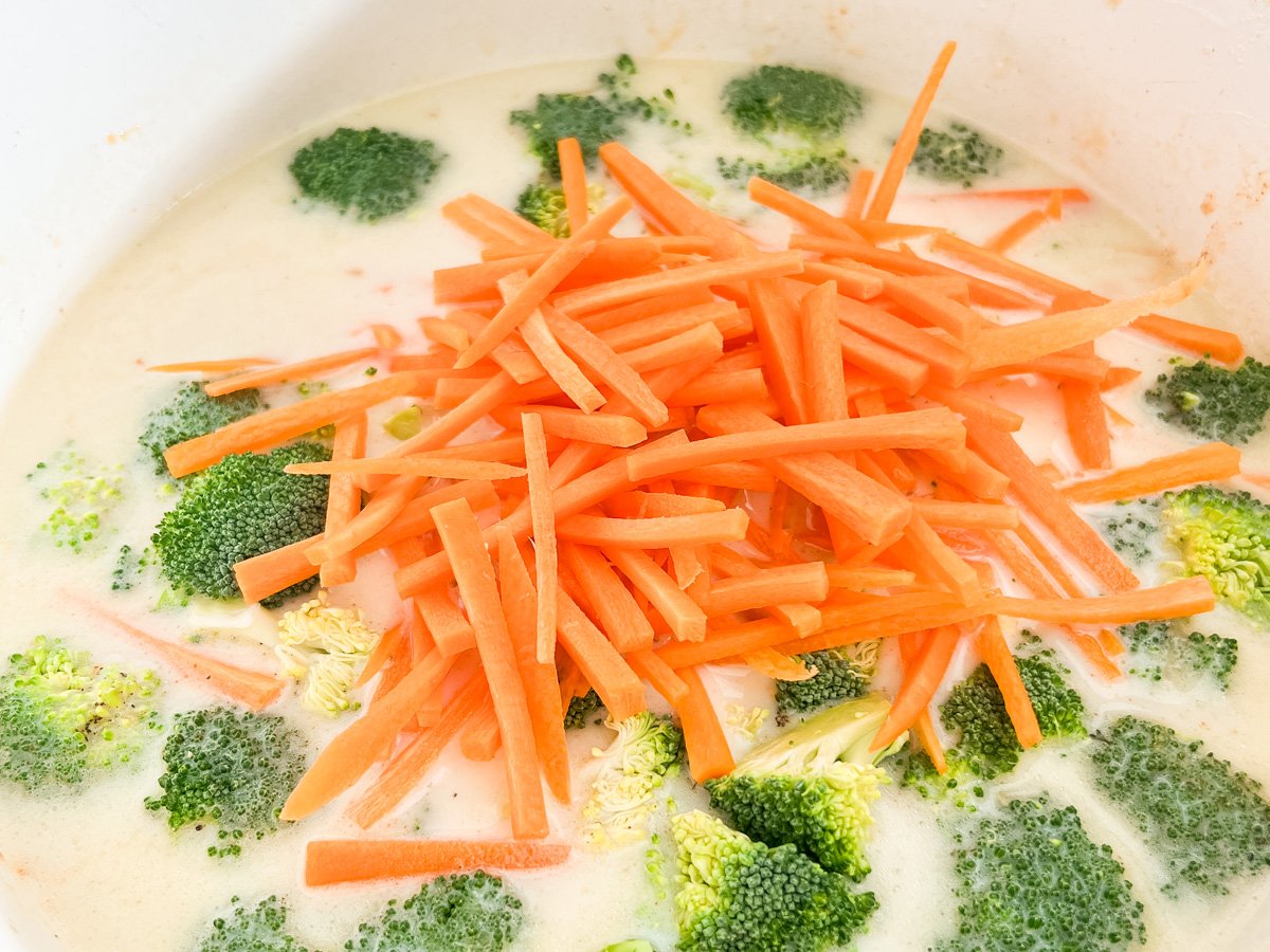 Broccoli florets and julienned carrots added to the creamy soup base before simmering.