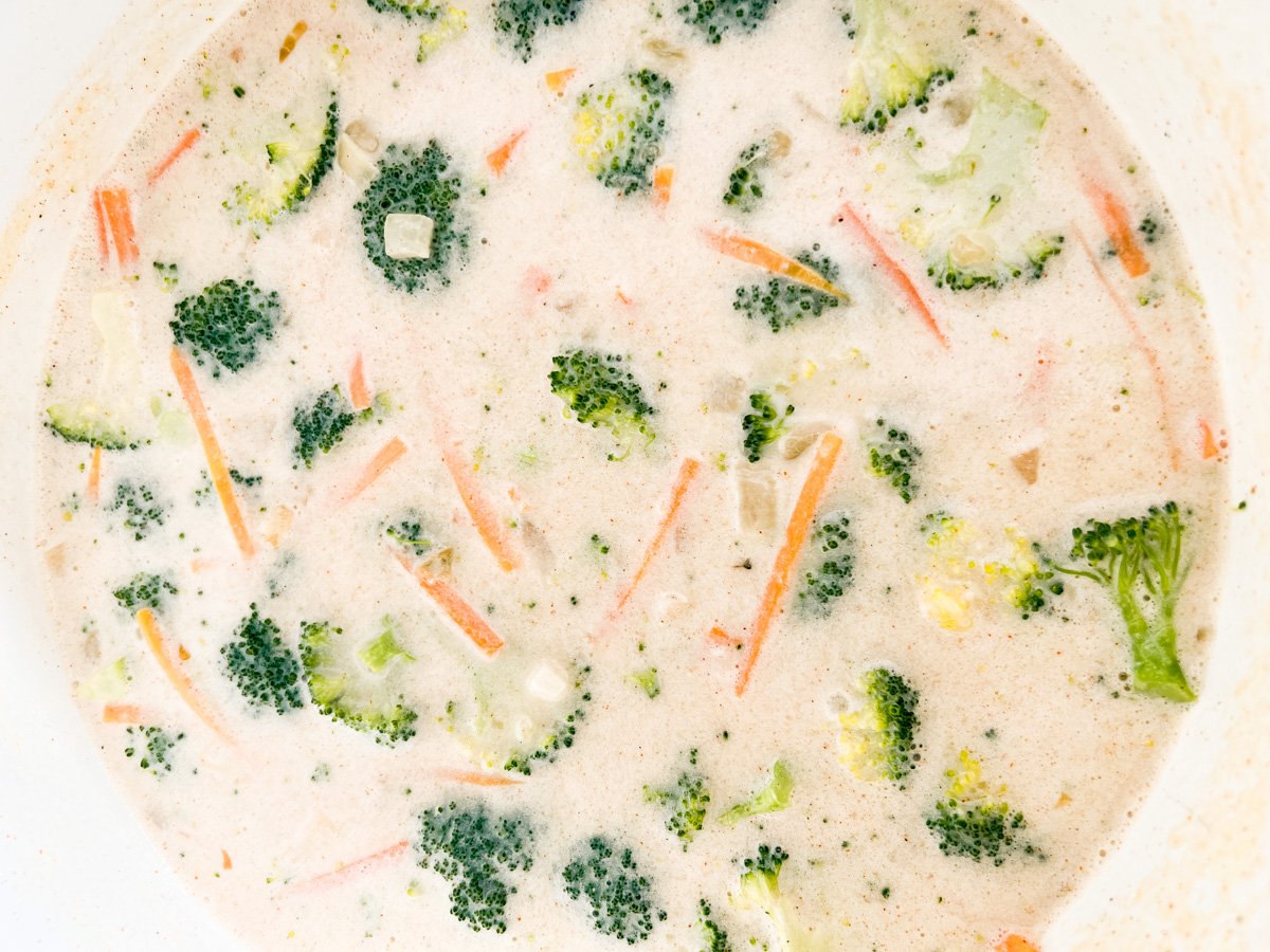 Simmered soup with visible broccoli and carrots in a creamy broth just before adding cheese.