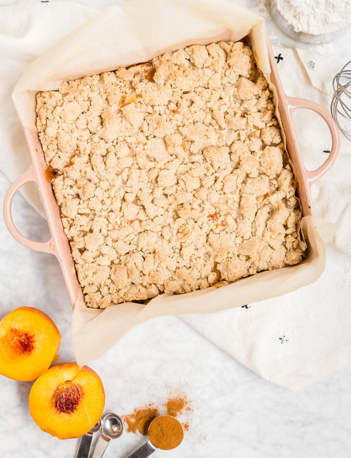 An aerial view of a baking dish with gluten-free vegan peach crumb bars in it and fresh peaches next to it. 