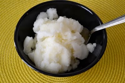 A black bowl with lemon sorbet and spoon in it on a yellow placemat.