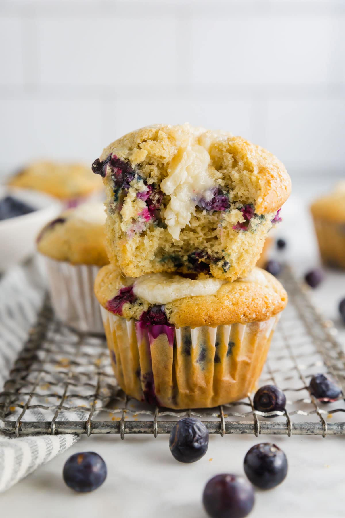A photo of two gluten-free blueberry cheesecake muffins stacked on top of each other. The top one has a bite taken out of it.