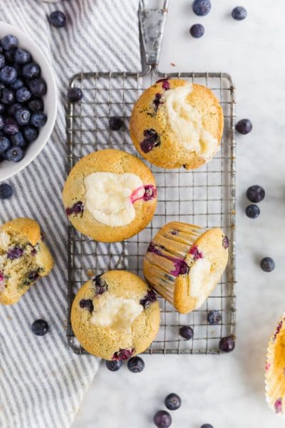 An overhead photo of gluten-free blueberry cream cheese muffins on a wire cooling rack with fresh blueberries surrounding them.