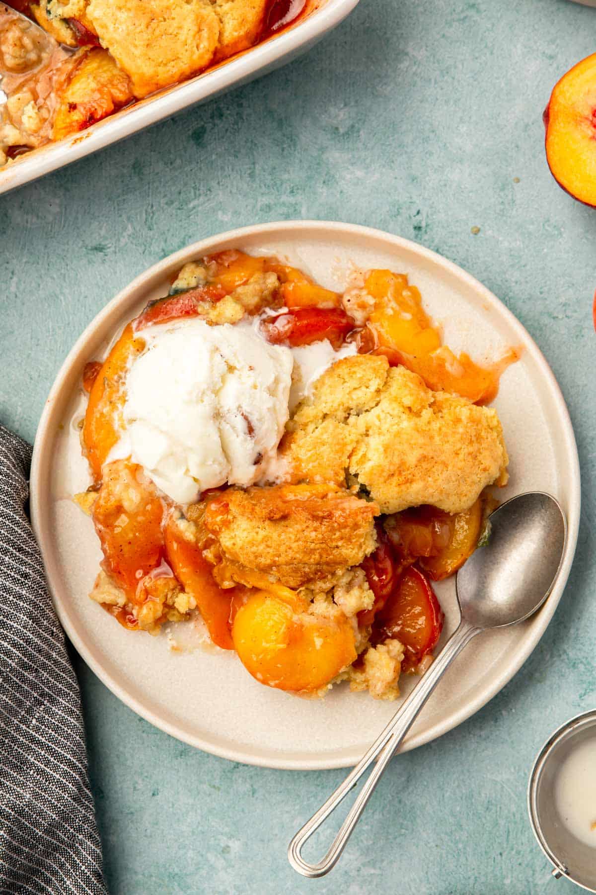 An overhead view of a plate of peach cobbler topped with ice cream with a spoon.