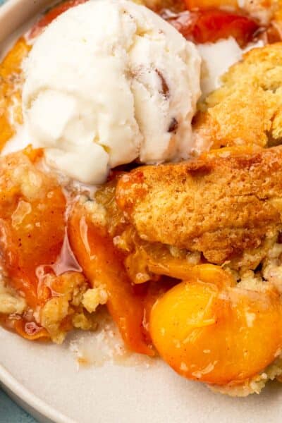 A closeup of a serving of gluten-free peach cobbler topped with a scoop of vegan ice cream.