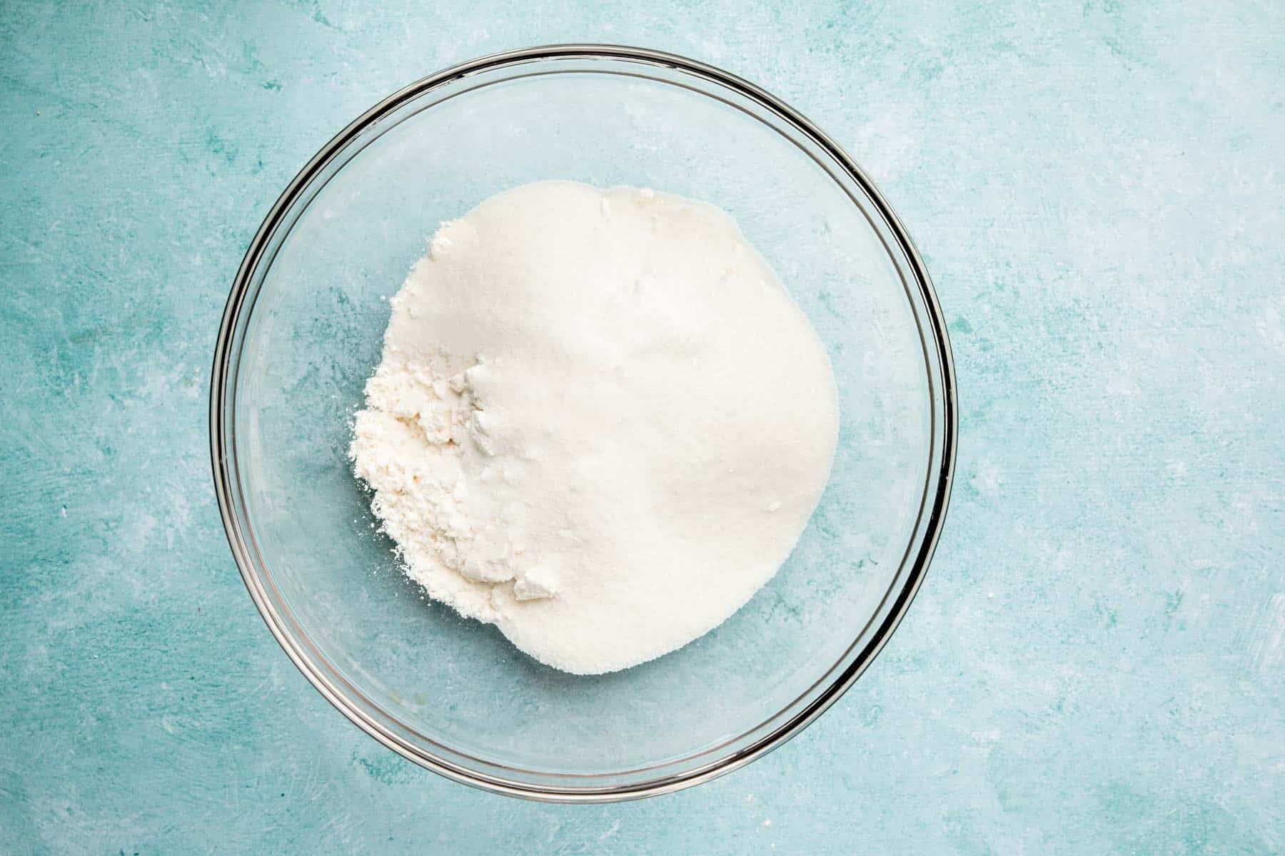 A glass mixing bowl with granulated sugar and gluten-free flour blend before mixing.