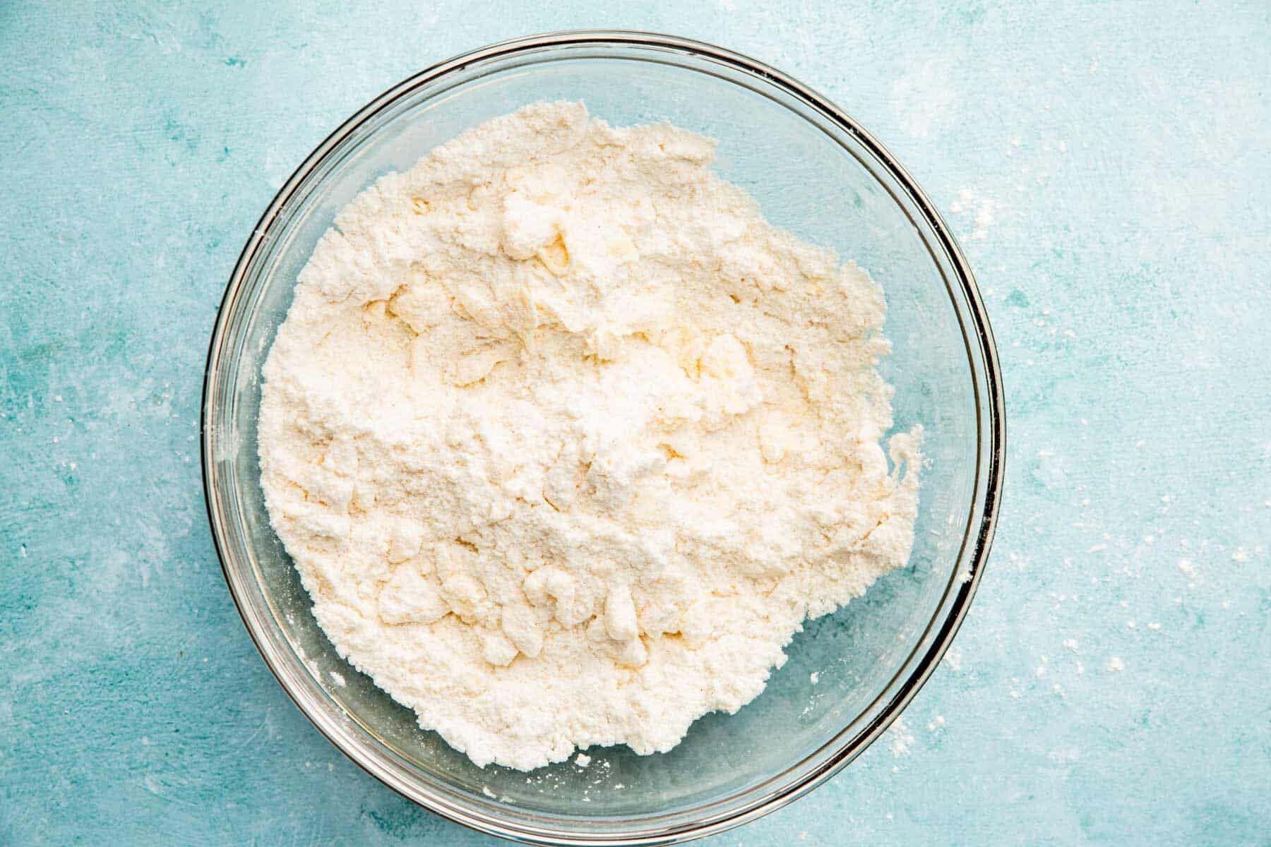 A glass mixing bowl with gluten-free flour and cold butter mixed in.