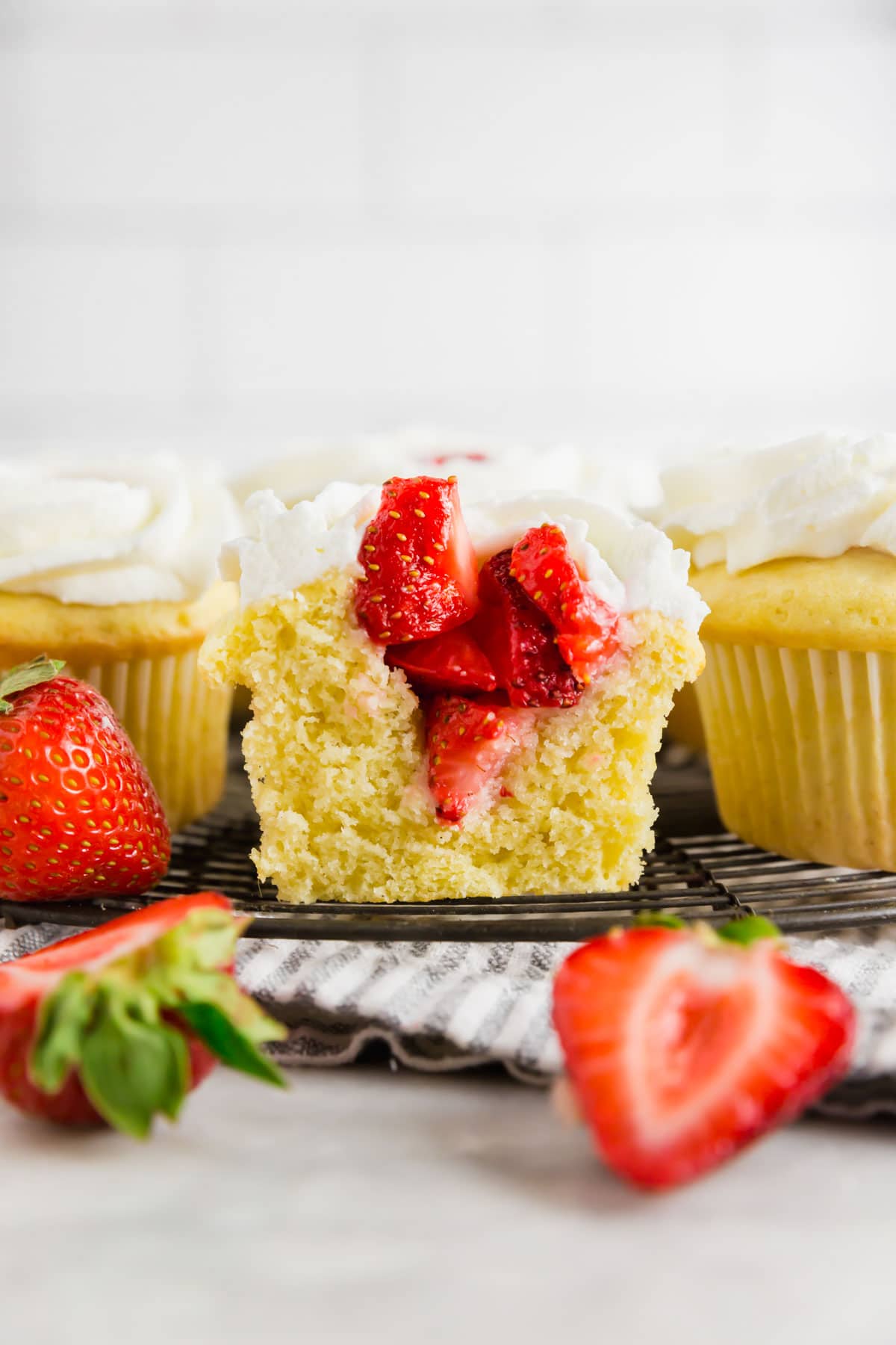 A strawberry shortcake cupcake sliced in half to show the strawberry filling on top of a wire cooling rack.