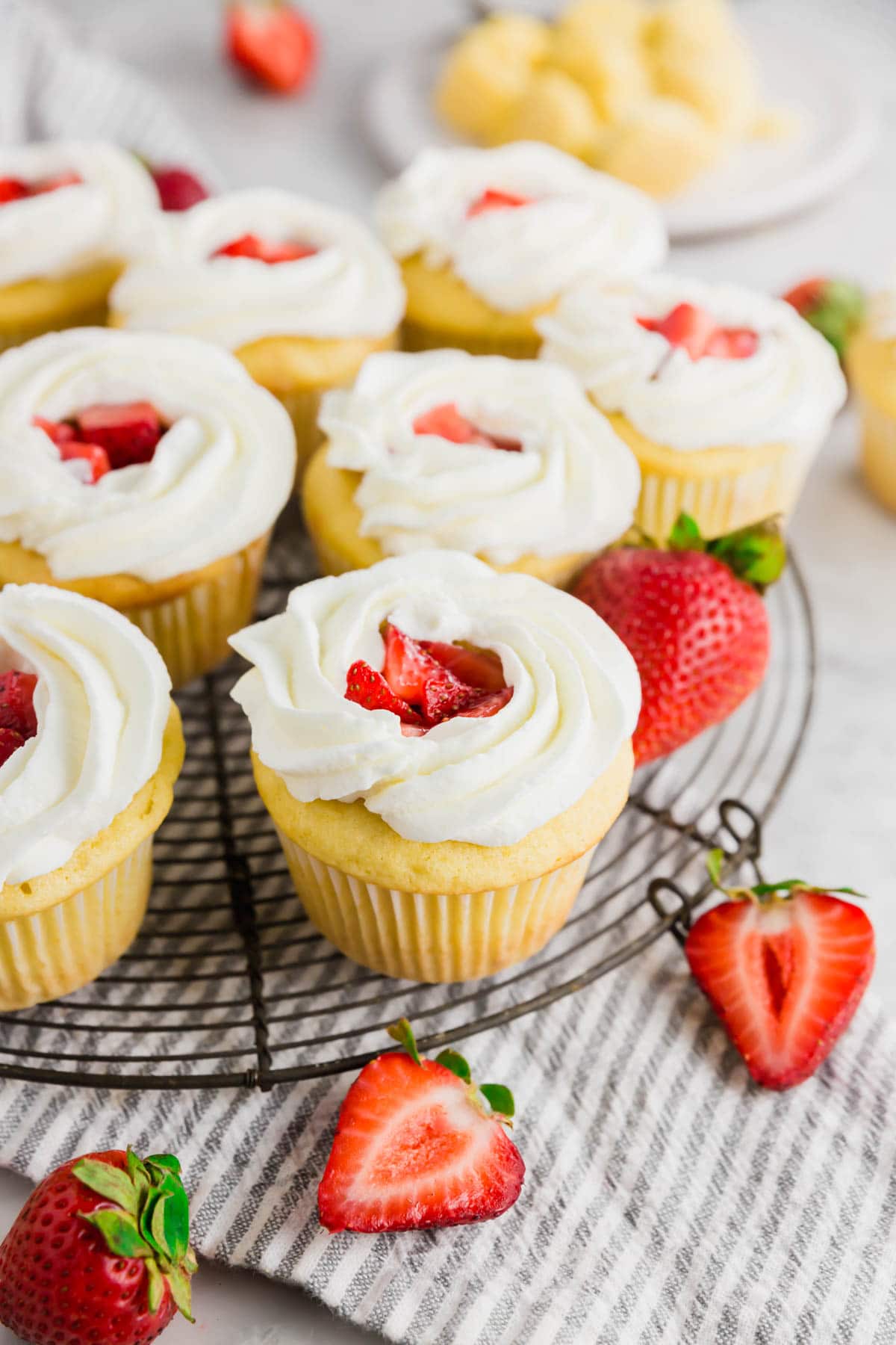 A wire cooling rack with gluten-free strawberry shortcake cupcakes on it topped with fresh whipped cream.