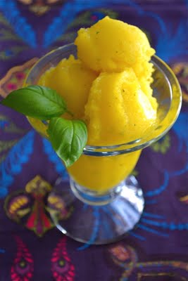 A glass bowl with mango sorbet topped with basil leaves.