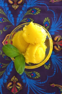 A glass bowl with mango basil sorbet topped with basil leaves on a floral table cloth.