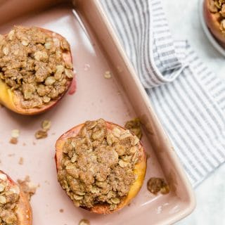 Aerial view of a pink baking dish filled with halved peaches stuffed with gluten-free streusel topping.