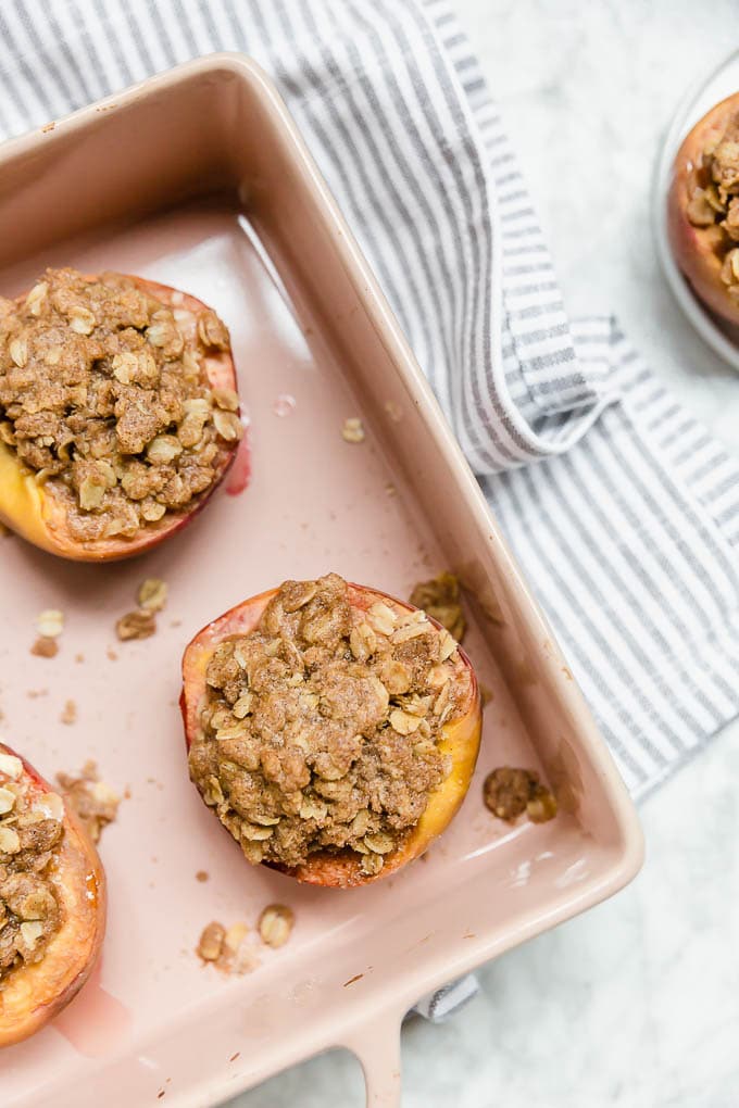 Aerial view of a pink baking dish filled with halved peaches stuffed with gluten-free streusel topping.