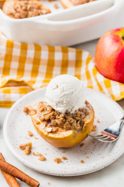 A photo of baked apple topped with ice cream and gluten-free streusel on a plate.