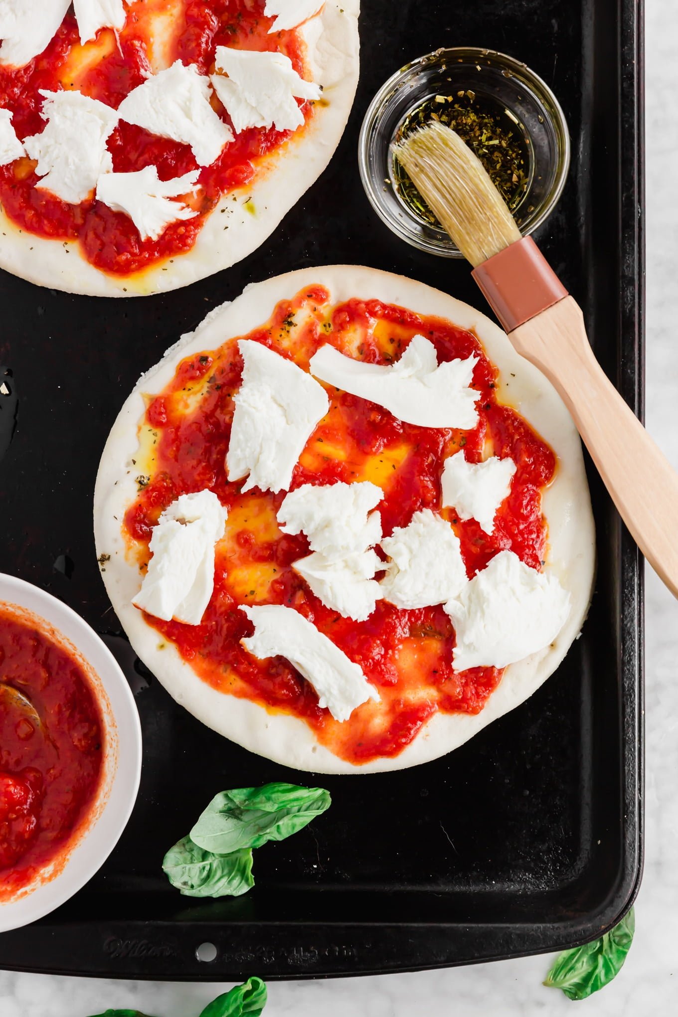 An aerial photo showing pita bread topped with marina sauce and fresh mozzarella to make pita pizzas.