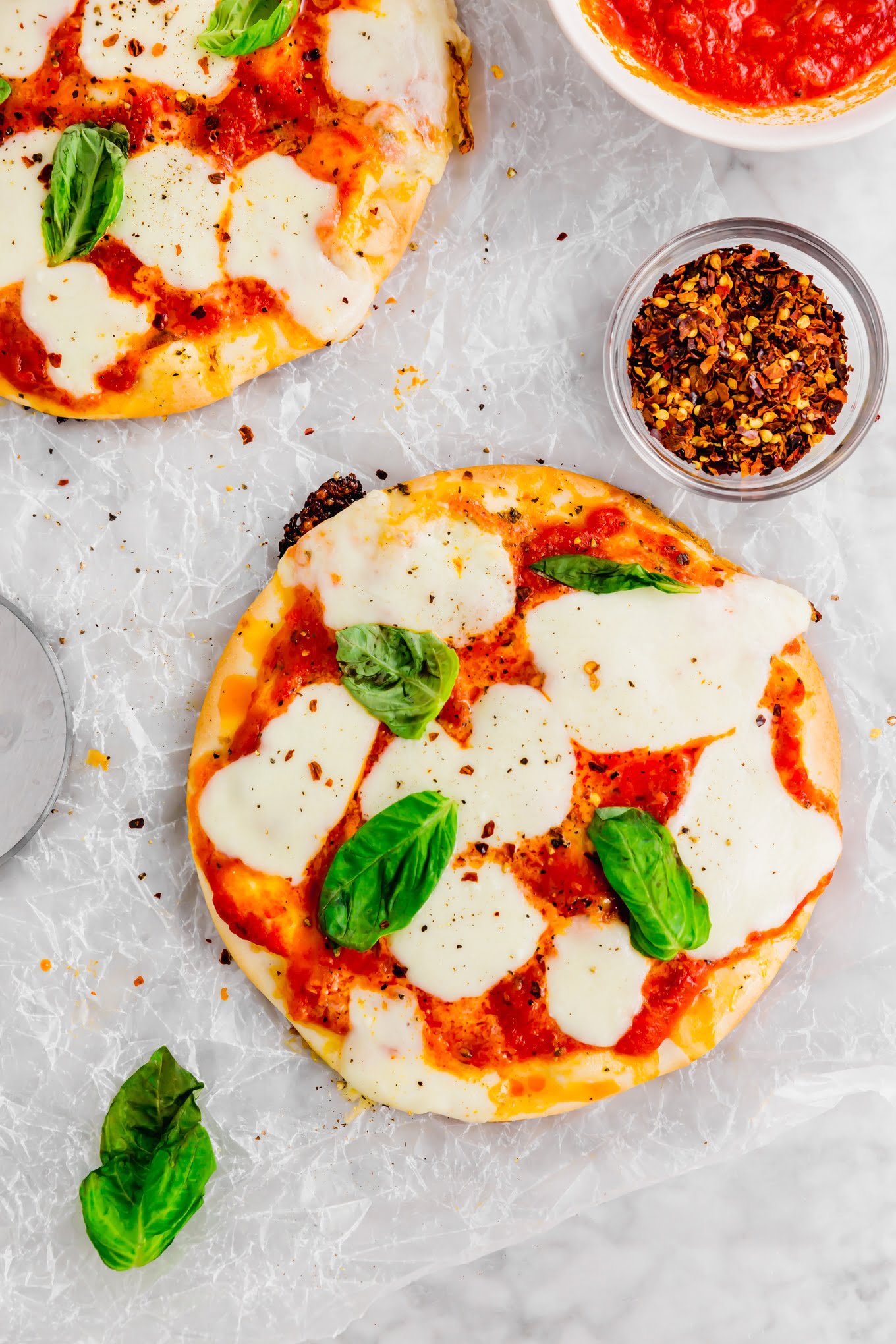 A photo of two gluten-free pita pizzas topped with fresh mozzarella and basil on parchment paper.