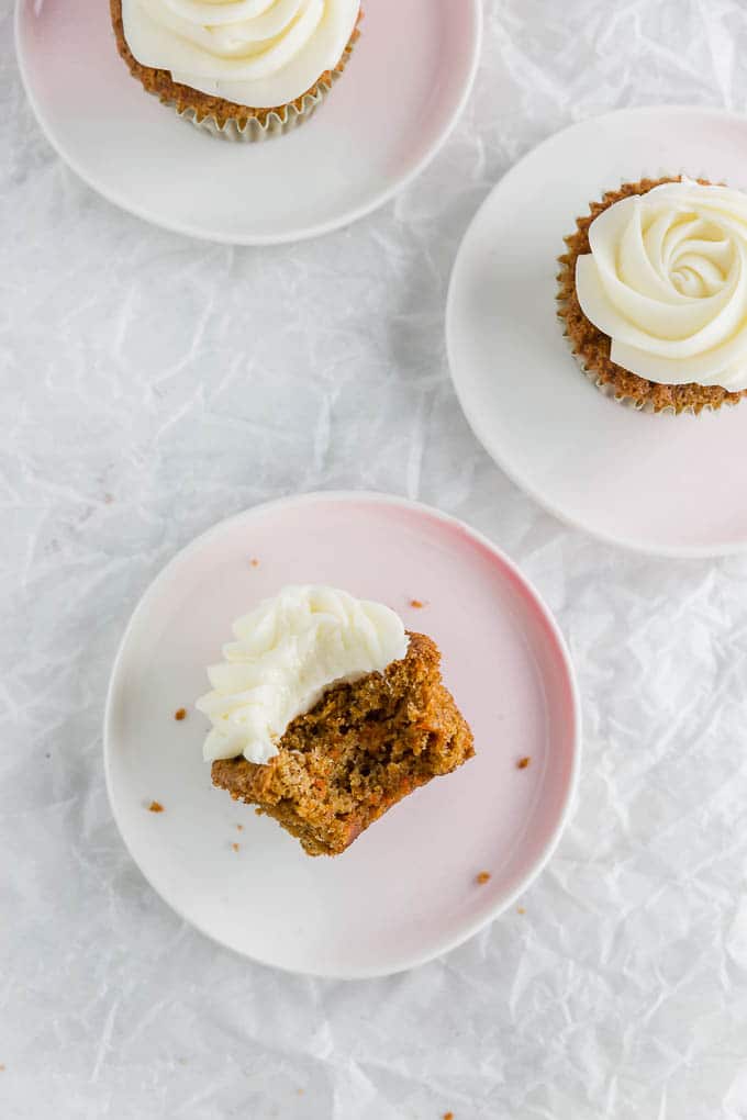 A photo of gluten free carrot cake cupcake on a plate with a bite taken out.