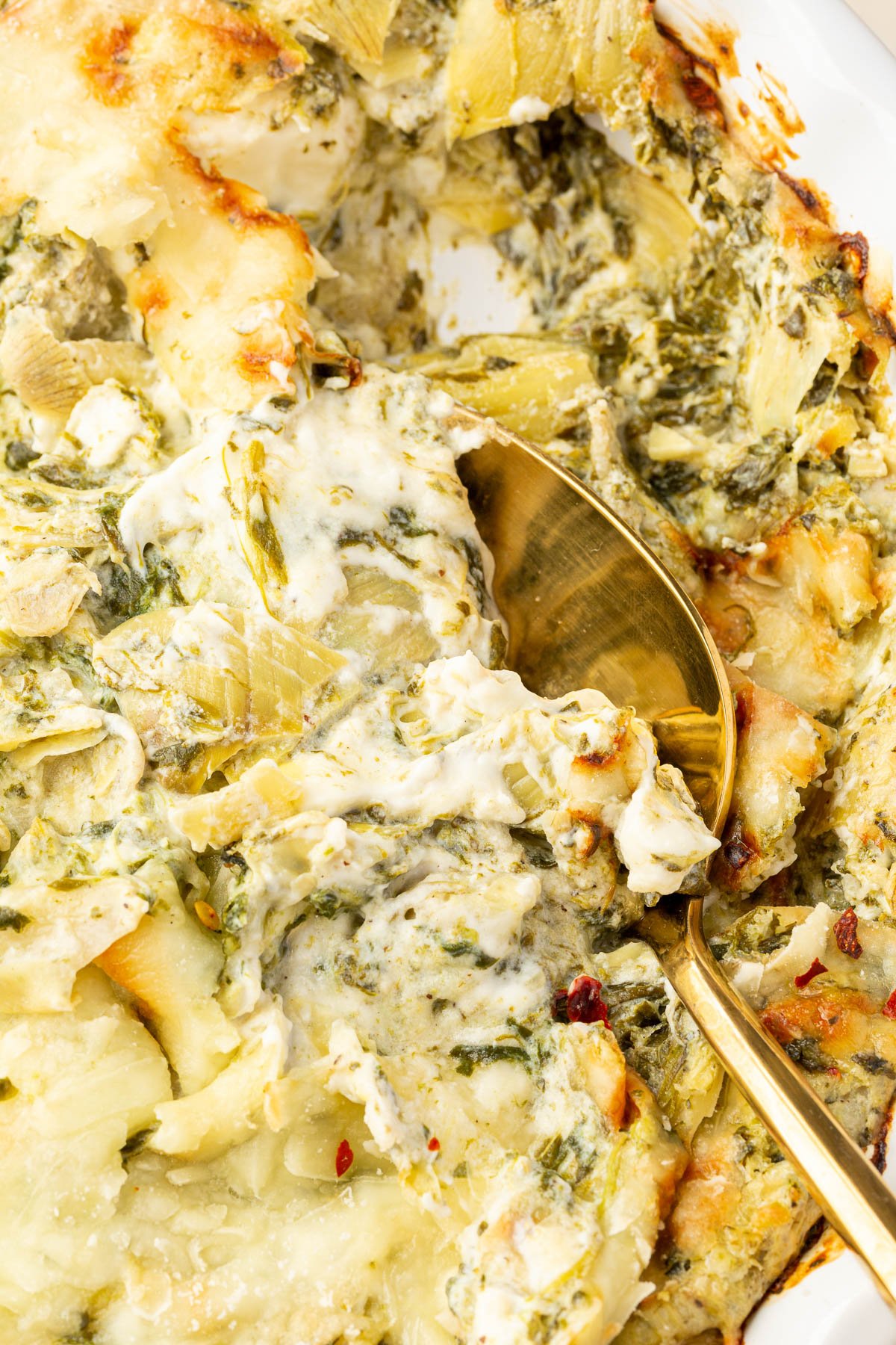 Close up image of cooked spinach artichoke dip with a spoon in it.