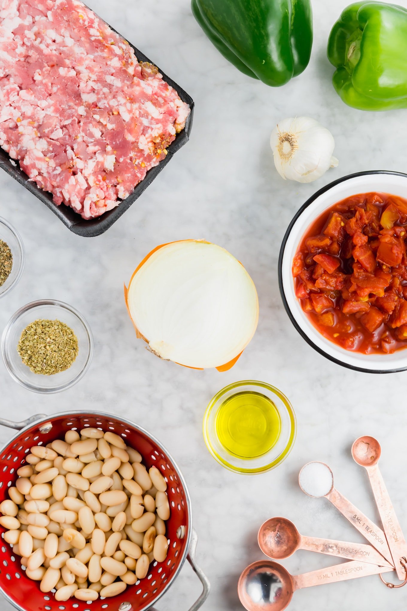 A photo of raw italian sausage, crushed tomatoes, onion, beans, olive oil, herbs, spices, and garlic ready to make white bean italian sausage stew. 