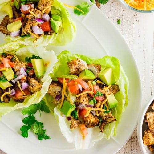 A plate with three chicken taco lettuce wraps with cilantro and ingredients surrounding the plate.