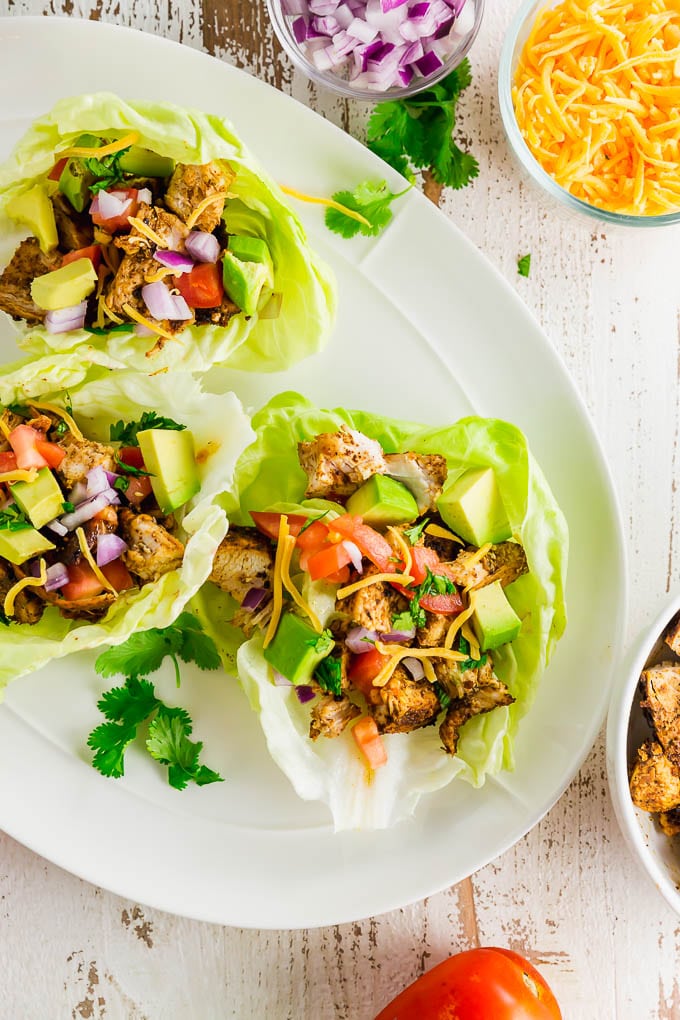 A plate with three chicken taco lettuce wraps with cilantro and ingredients surrounding the plate. 